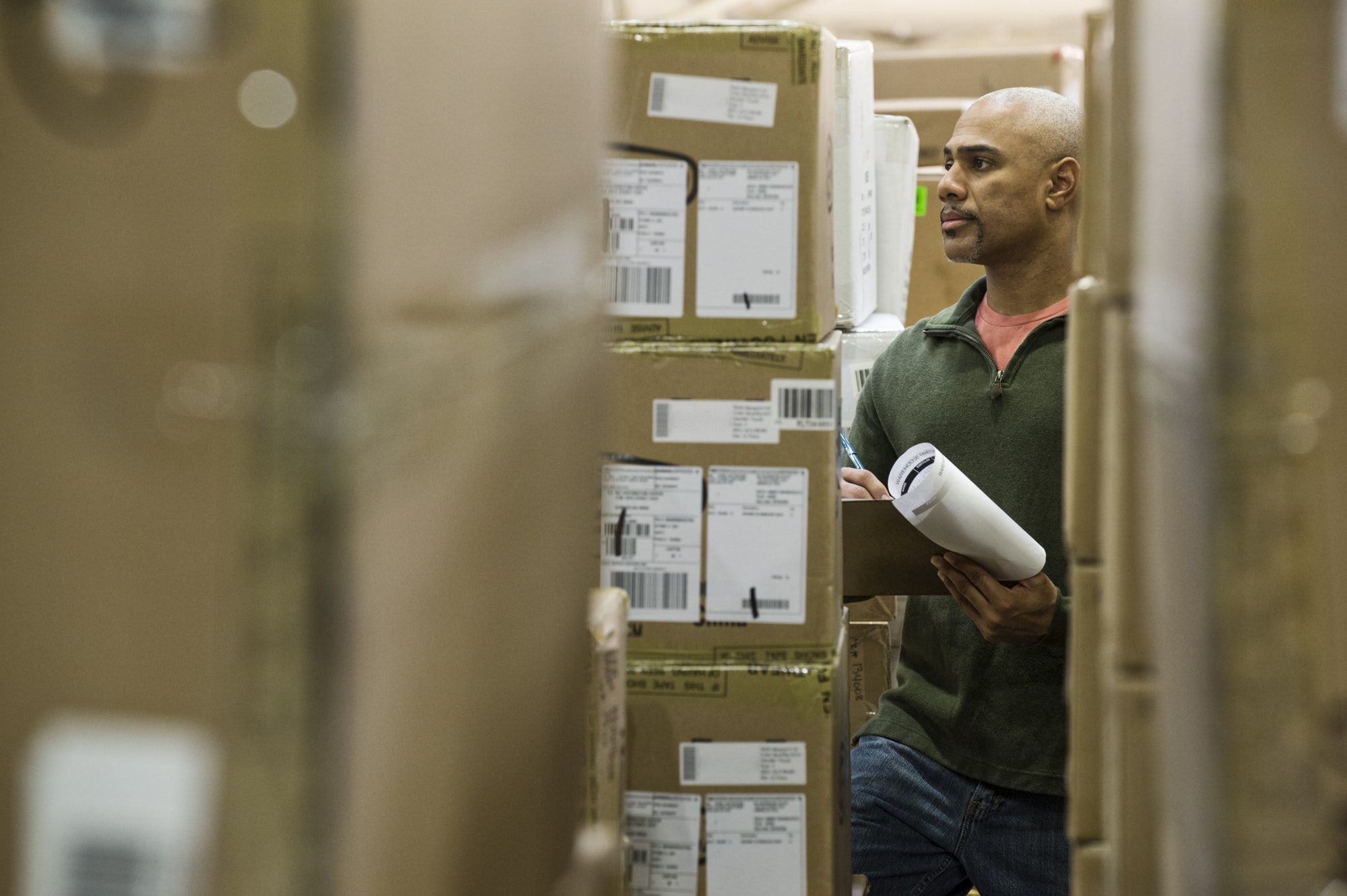 A black warehouse worker keeping track of boxed inventory in a distribution warehouse.